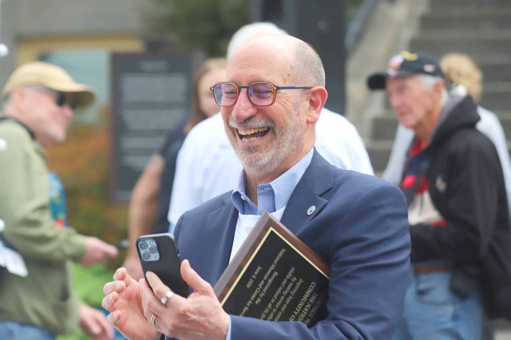 Edmonds Mayor Mike Rosen takes a photo while holding a plaque honoring Edmonds as the nations first community of service during a launch for Edmonds Serves on Saturday in Edmonds. (Michael Henneke / The Herald)