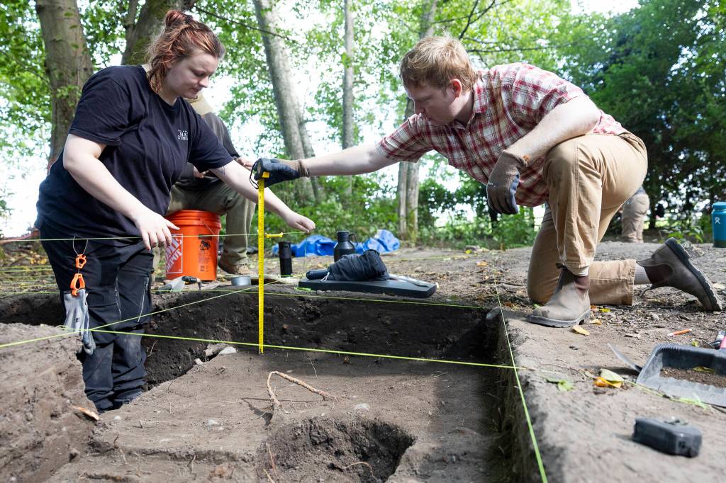 Toby Haaf and Ryan Babjak record measurements of their dig site on Tuesday, July 28, 2026 in Mukilteo, Washington. (Olivia Vanni / The Herald)