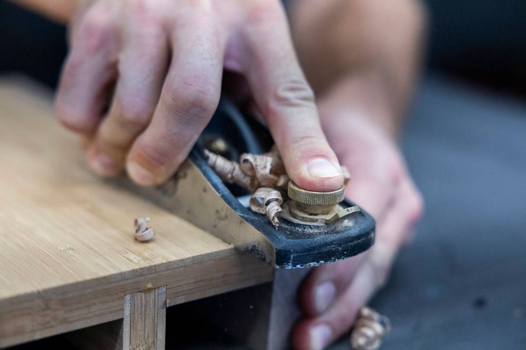 AJ Hansen trims the edges of a table leaf stand at the Bandpass Design workshop on July 28 in Edmonds, Washington. (Olivia Vanni / The Herald)
